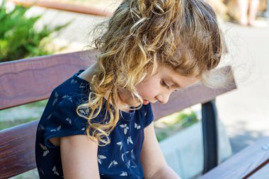 Yürümekte olan kız bir bankta kambur duruyor. Kötü vücut duruşu.