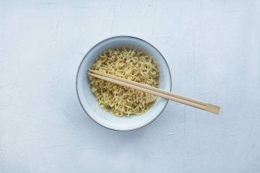 Beyaz desenli arka planda ahşap çubuklarla dolu bir kasede hazır şehriye. Düzen, düzlük, kopyalama alanı, üst görünüm. Seçici odak.