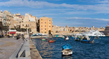 Senglea, Malta - 7 Mart 2017: Valletta ufuk çizgisine bakan güneşli bir günde geleneksel balıkçı tekneleri ve yatlarıyla Senglea limanı