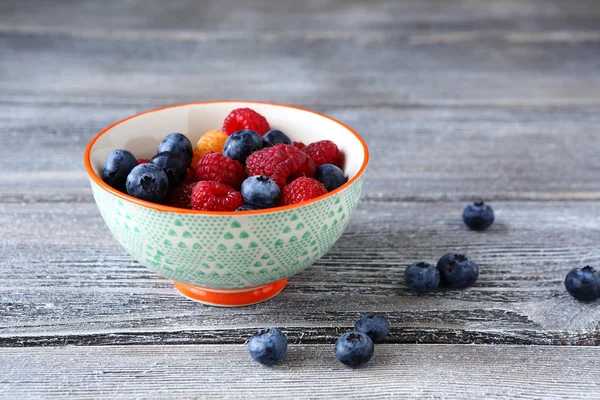 Raspberries and blueberries in a bowl on boards — Stock Photo, Image