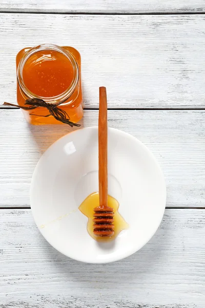 Tarro de miel dulce con un palo en el plato — Foto de Stock