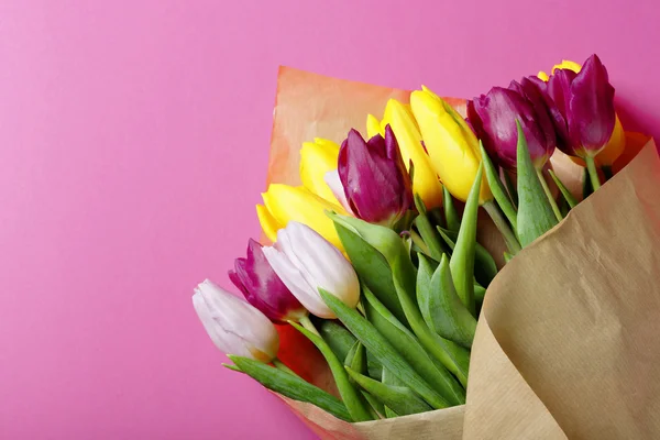 Tulpen in braunem Papier auf rosa Hintergrund — Stockfoto