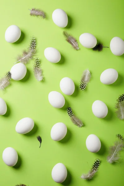 Ovos brancos e penas sobre fundo verde — Fotografia de Stock