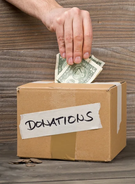 L'uomo mette denaro in donazioni scatola di cartone con banconota da un dollaro — Foto Stock
