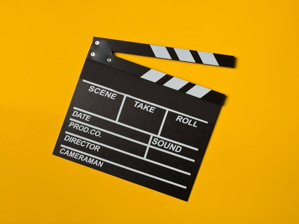 Single, black, opened movie clapper or clapper-board flat lay top down view from above on yellow or orange background