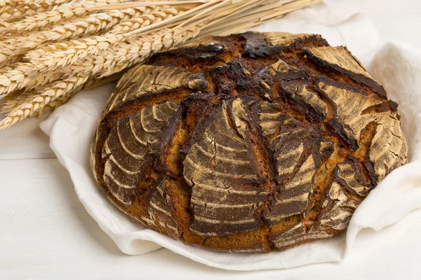 Hand made bread loaf with wheat ears on white wood — Stock Photo, Image