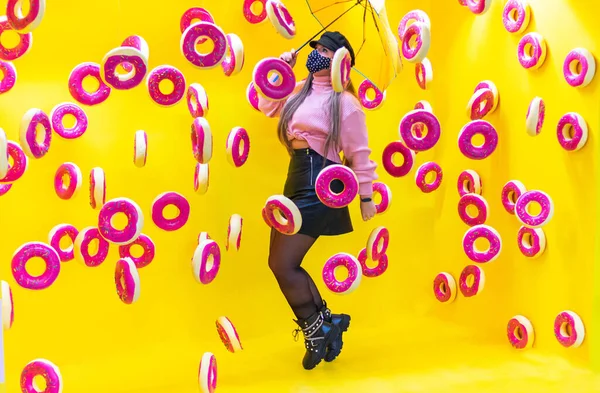 a young woman with umbrella and mask between flying donuts