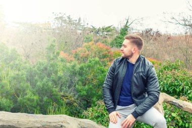 Moda giyinmiş genç bir adam ağaçlar arasında sonsuzluğa bakıyor.