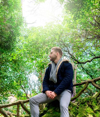 Parktaki bir merdivenin korkuluğuna yaslanan genç bir adam.