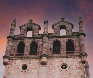 Günbatımı gökyüzü olan bir ortaçağ kilise kulesi.