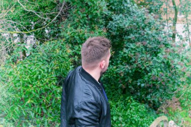 Arka planda ağaçlar olan bir yandan genç adamın yakın portresi.