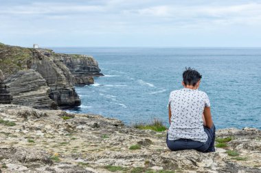 Bir uçurumdan denize bakan genç bir kadın.