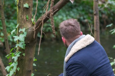 Genç bir adam ormanda sırtüstü sonbaharda nehri seyrediyor.
