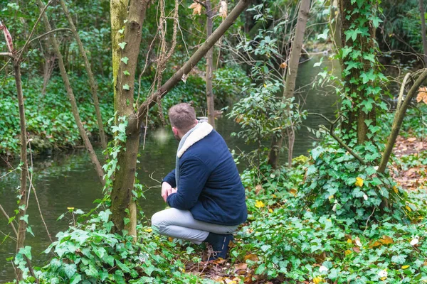 a young man on his back and crouching in the forest looking at the river in autumn