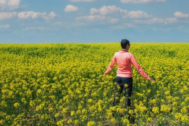 Sarı çiçek tarlasının ortasında bir kadın yürüyüşçü.