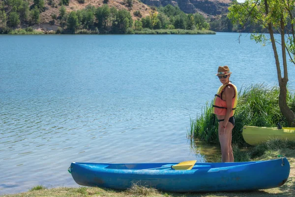 a woman in a life jacket standing next to a canoe near the water