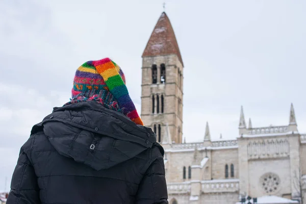 a woman in warm clothes and her back turned contemplating a medieval church in winter
