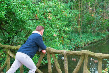 Köprüde taş parmaklıklarla poz veren genç bir adam.