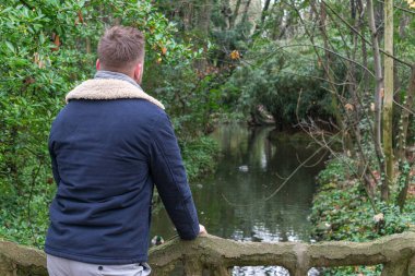 Köprüde taş parmaklıklarla poz veren genç bir adam.