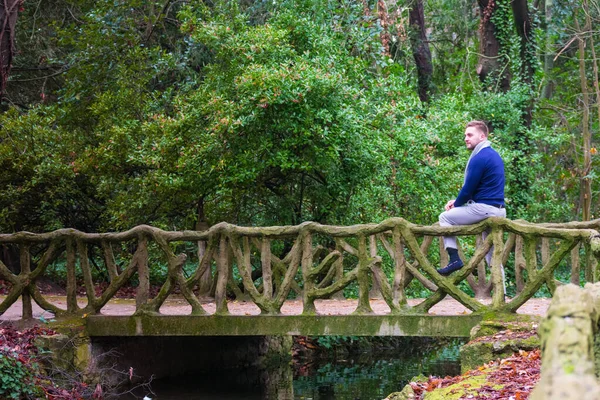 Köprüde taş parmaklıklarla oturan genç bir adam.