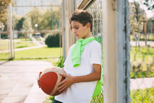 Potret seorang remaja lucu dengan bola basket di tangannya. Anak itu memegang bola di tangannya dan melihatnya. Olahraga, pendidikan, kesenangan — Stok Foto