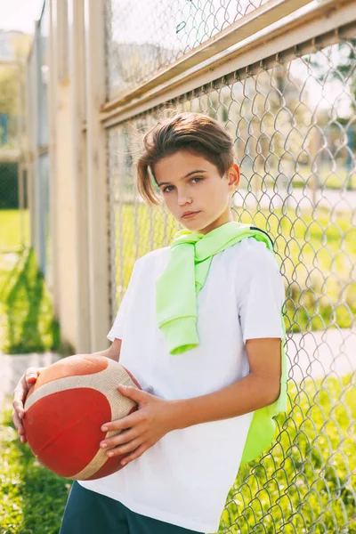 Seorang remaja cantik memegang bola basket di tangannya dan melihat ke kamera. Potret seorang anak laki-laki dengan bola di tangannya. Olahraga, pendidikan, kesenangan — Stok Foto