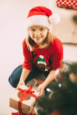 Güzel kız Noel ağacının yanında yerde oturuyor ve elinde bir hediye tutuyor. Noel ve Yeni Yıl konsepti. Tatil, hediye, metin için yer