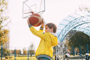 Spor üniformalı şirin bir çocuk elinde bir basketbol topu tutuyor ve fırlatmaya hazırlanıyor.