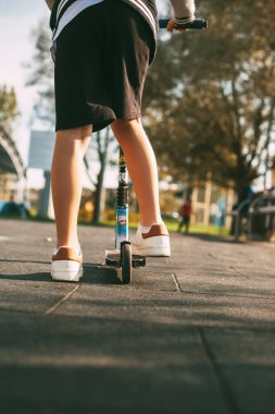 Yakın plan, scooter süren bir çocuğun bacağı. Aktif eğlence, sağlıklı yaşam tarzı, açık hava eğlencesi.