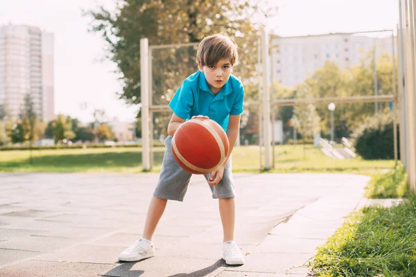 Atlet imut yang fokus memimpin bola dalam permainan basket. Anak laki-laki bermain basket sepulang sekolah. Olahraga, gaya hidup sehat, rekreasi — Stok Foto