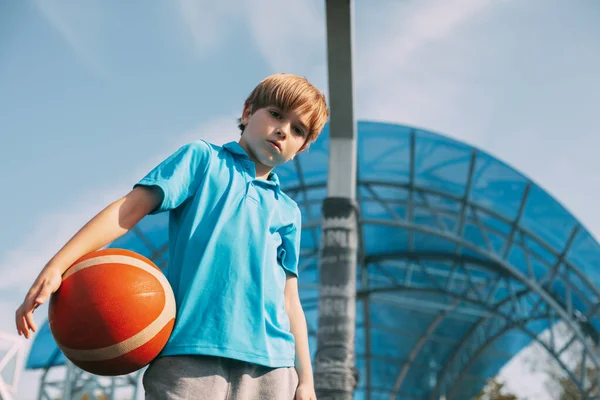 Potret seorang anak laki-laki dalam seragam olahraga dengan bola basket di tangannya. Seorang anak laki-laki memegang bola di tangannya setelah bermain basket. Olahraga, pendidikan, gaya hidup sehat — Stok Foto