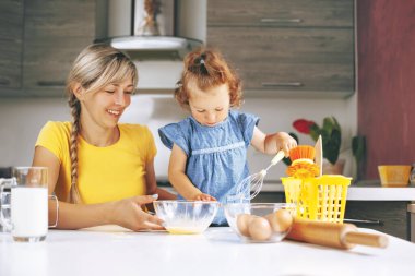 Mutlu anne ve küçük kızı mutfakta yemek pişiriyorlar. Kız çırpıcıyla cam bir kasede yumurta çırpıyor. Aile tatili kavramı