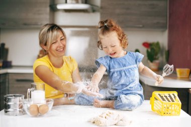 Çekici küçük bir kız masada oturuyor ve annesiyle un ile oynuyor, hamurun yanında ve malzemeler duruyor. Aile dinlenme konsepti, metin için yer