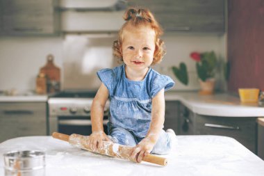 Mutlu bir kız masada oturuyor ve hamuru oklavayla yuvarlıyor. Kız un ile kirlenmişti ve... Aile yemekleri, aile tatilleri.