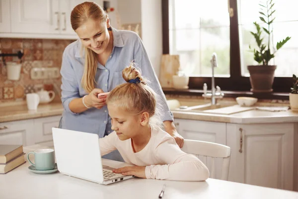 Mamá ayuda a su hija a hacer sus deberes en la cocina con un ordenador portátil en Internet, habla con el maestro. Educación a distancia, educación en línea, concepto de educación en el hogar —  Fotos de Stock