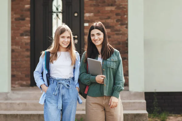 Krásné usměvavé studentky s batohy a tablet jít z domova na univerzitu, dvě dívky zblízka, Technologie, vzdělávání, volný čas koncept — Stock fotografie