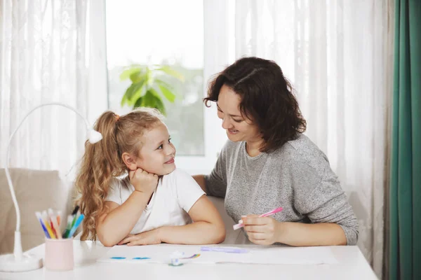 妈妈帮助她的小女儿做作业。妈妈教女孩画画。家庭培训、在线培训 — 图库照片