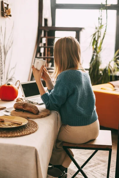 A young woman enjoys coffee in the morning and works at her laptop. Work at home, online business, freelance. Rear view — Stock Photo, Image