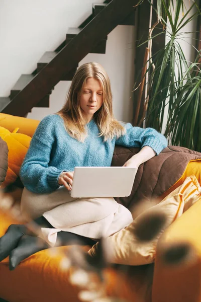 Jovem usa laptop, verifica e-mail notícias on-line sentado no sofá. Menina bonita trabalhando em um computador, assistindo a um webinar, estudando em casa — Fotografia de Stock