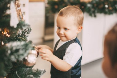 Takım elbiseli komik küçük bir çocuk Noel ağacını süslüyor. Tatil, etkinlik, Noel ve Yeni Yıl