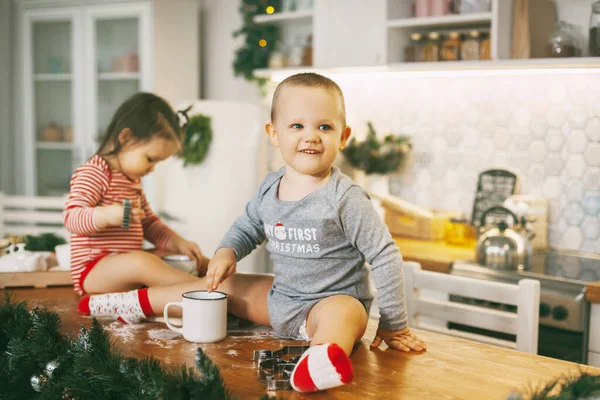 Funny kids sit on the kitchen table and play with cookie cutters. Children help bake cookies for Christmas and New year — Stock Photo, Image
