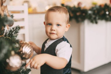 Takım elbiseli komik küçük bir çocuk Noel ağacını süslüyor. Tatil, etkinlik, Noel ve Yeni Yıl