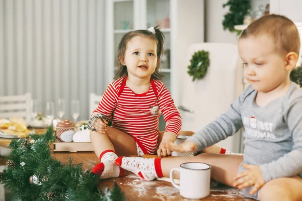 Funny kids sit on the kitchen table and play with cookie cutters. Children help bake cookies for Christmas and New year — Stock Photo, Image