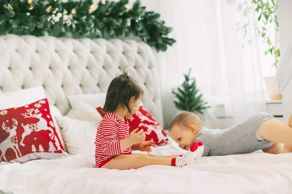 En liten pojke och flicka leker på sina föräldrars säng på juldagsmorgonen. Familj morgon på en snöig kall juldag — Stockfoto