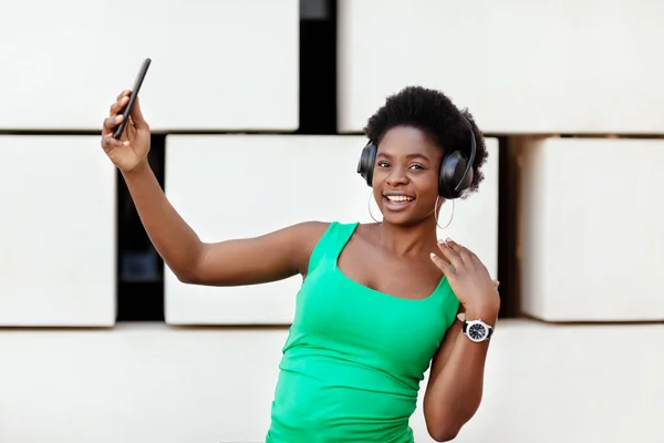 Menina africana bonita ouvindo música em fones de ouvido sem fio em seu telefone celular, dançando e tirando selfies. — Fotografia de Stock