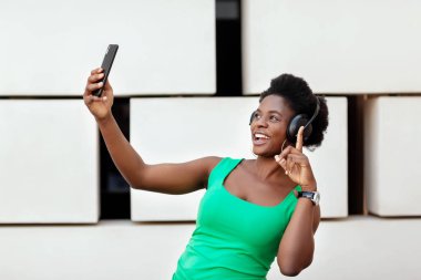 Güzel Afrikalı kız cep telefonunda kablosuz kulaklıkla müzik dinliyor, dans ediyor ve selfie çekiyor..