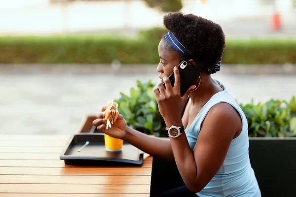 Mulher africana bonito almoçar ao ar livre no café da cidade. Uma menina está falando ao telefone durante o almoço. — Fotografia de Stock