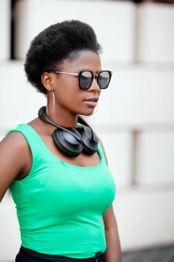 Güneş gözlüklü ve sokakta yeşil tişörtlü genç bir Afrikalı kızın portresi.