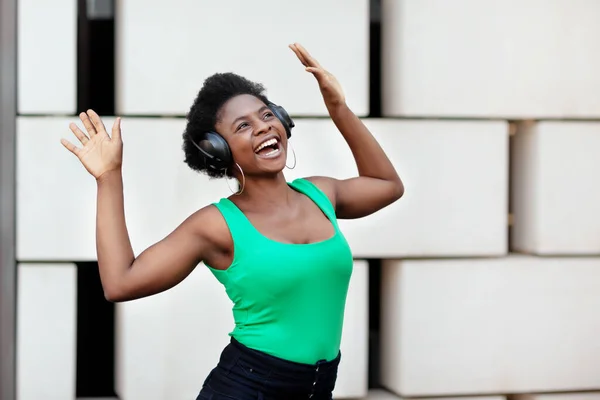Mulher africana sorri, ouve música com fones de ouvido e danças na rua — Fotografia de Stock