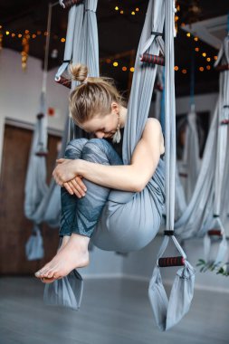 Genç bir kız modern bir stüdyoda yoga çalışmasından sonra dinleniyor. Bir kız yerçekimsiz hava yogası için hamakta oturuyor. Uyum, farkındalık ve sağlıklı bir yaşam tarzı. Metin için boşluk